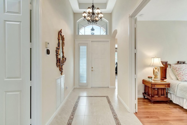 foyer with an inviting chandelier, a raised ceiling, visible vents, and baseboards