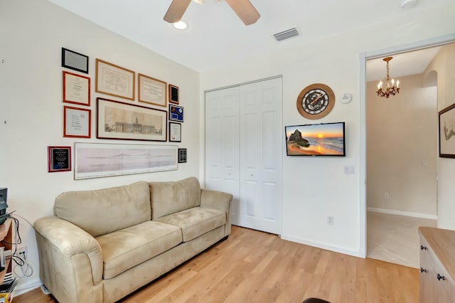 living area featuring baseboards, visible vents, light wood finished floors, and ceiling fan with notable chandelier