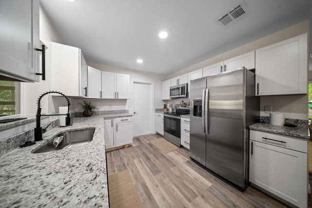 kitchen featuring light wood-style flooring, stainless steel appliances, a sink, visible vents, and white cabinetry