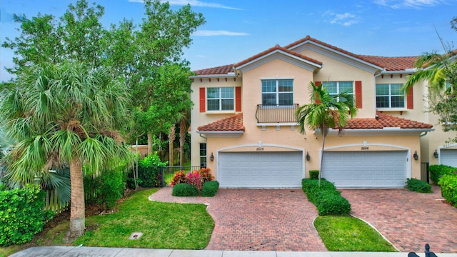 mediterranean / spanish house featuring a garage, a tile roof, decorative driveway, and stucco siding