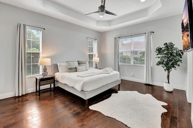 bedroom featuring ceiling fan, a raised ceiling, dark wood finished floors, and baseboards