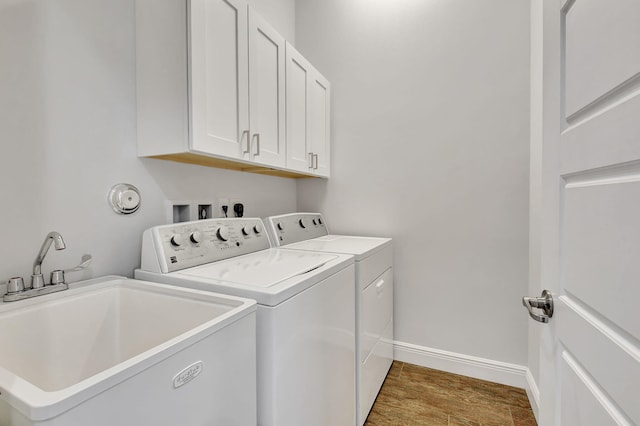 laundry area featuring wood finished floors, a sink, baseboards, cabinet space, and washer and clothes dryer