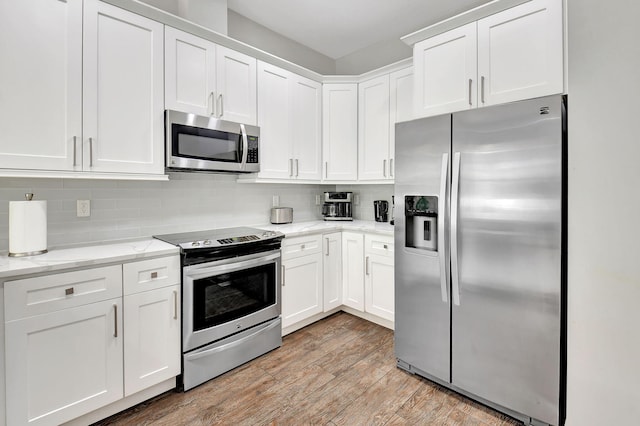 kitchen featuring light stone counters, stainless steel appliances, light wood-style floors, white cabinets, and decorative backsplash