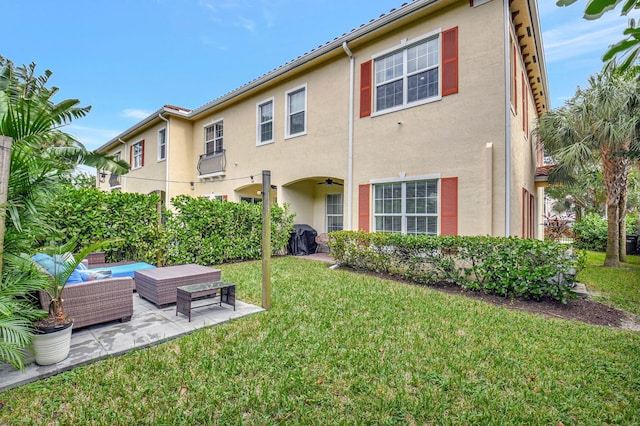 rear view of property with ceiling fan, a patio, an outdoor living space, a yard, and stucco siding