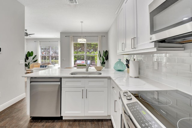 kitchen featuring light stone counters, a peninsula, hanging light fixtures, stainless steel appliances, and white cabinetry