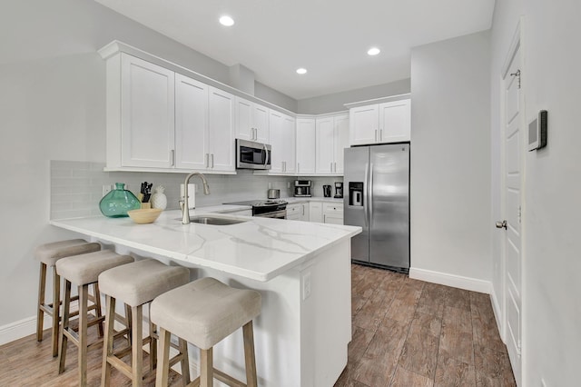 kitchen with stainless steel appliances, white cabinetry, a sink, light stone countertops, and a kitchen bar