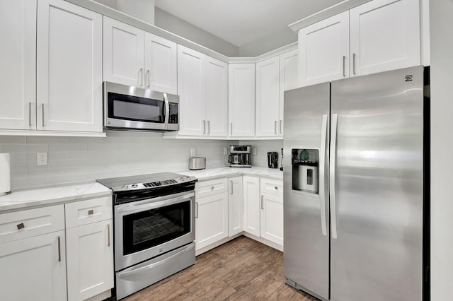 kitchen with stainless steel appliances, white cabinetry, and light stone countertops