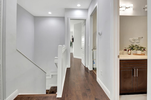 corridor featuring baseboards, dark wood-style floors, an upstairs landing, a sink, and recessed lighting