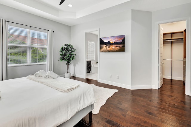 bedroom featuring baseboards, a raised ceiling, dark wood-type flooring, a walk in closet, and recessed lighting