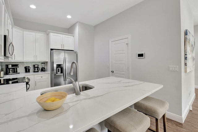 kitchen featuring light stone counters, stainless steel appliances, a sink, white cabinets, and a kitchen bar