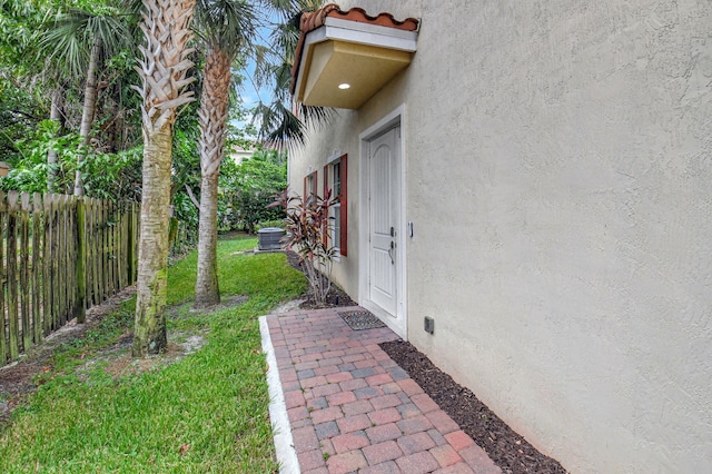 view of exterior entry featuring a yard, central AC unit, fence, and stucco siding