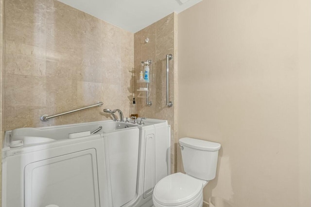 bathroom featuring a washtub, tile walls, washer / clothes dryer, and toilet