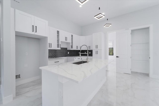 kitchen featuring a center island with sink, light stone countertops, sink, backsplash, and white cabinets