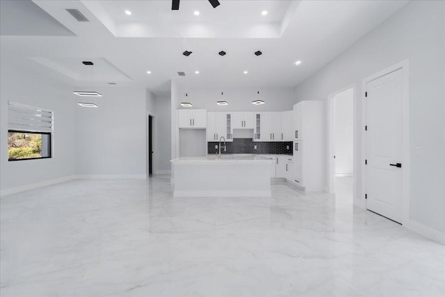 kitchen with a center island with sink, pendant lighting, a towering ceiling, ceiling fan, and white cabinets