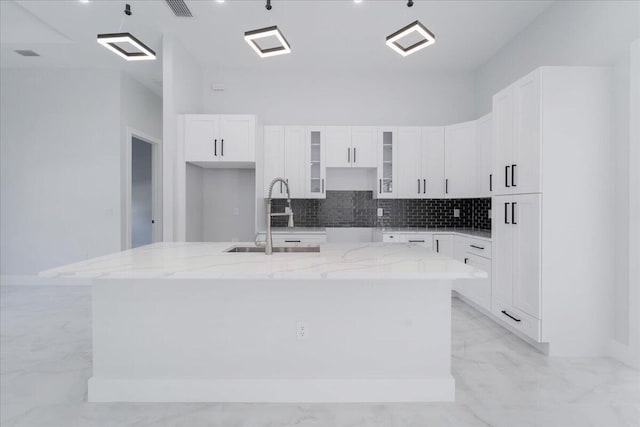 kitchen featuring a center island with sink, sink, light stone counters, and white cabinets