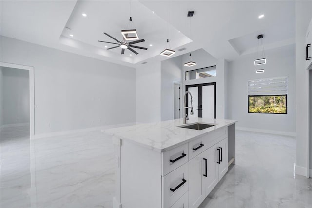 kitchen with a center island with sink, white cabinetry, pendant lighting, a raised ceiling, and light stone countertops