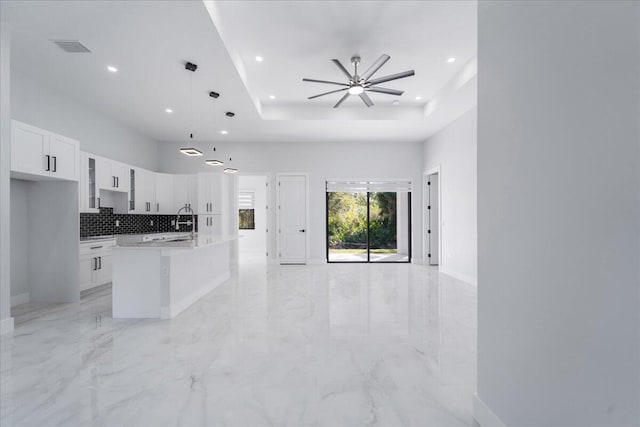 kitchen with a center island with sink, pendant lighting, a tray ceiling, ceiling fan, and white cabinets