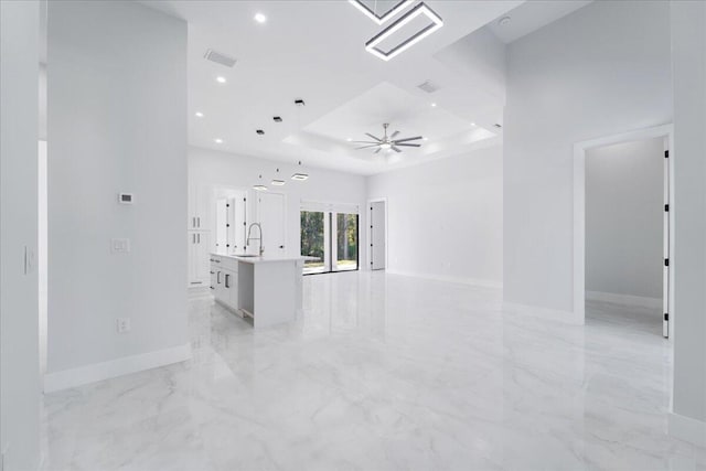 unfurnished living room with sink, ceiling fan, and a raised ceiling