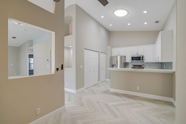 kitchen featuring kitchen peninsula, stainless steel appliances, light parquet flooring, high vaulted ceiling, and white cabinets