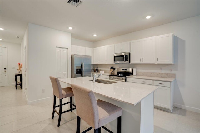 kitchen featuring a breakfast bar, stainless steel appliances, visible vents, a sink, and an island with sink