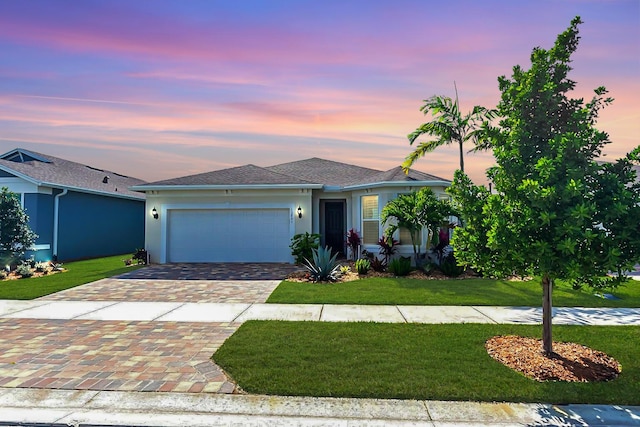 view of front facade with a garage, decorative driveway, a yard, and stucco siding