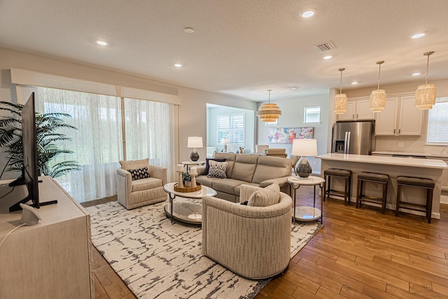 living area with light wood-type flooring, visible vents, a textured ceiling, and recessed lighting