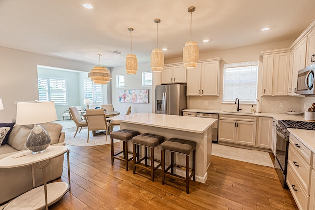 kitchen featuring stainless steel appliances, light countertops, hanging light fixtures, a sink, and a kitchen island