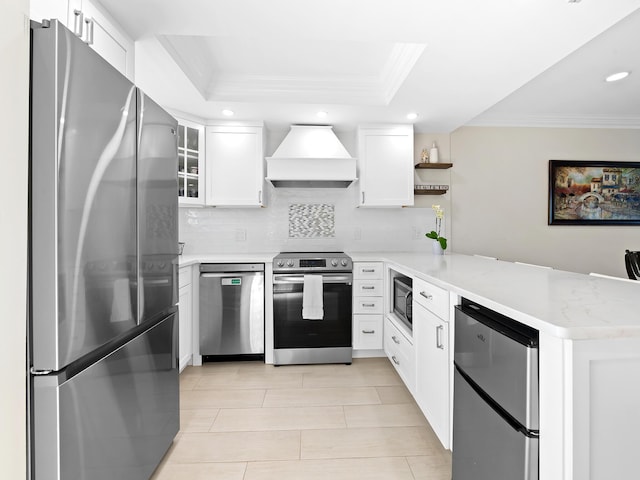 kitchen featuring appliances with stainless steel finishes, premium range hood, white cabinetry, a tray ceiling, and kitchen peninsula