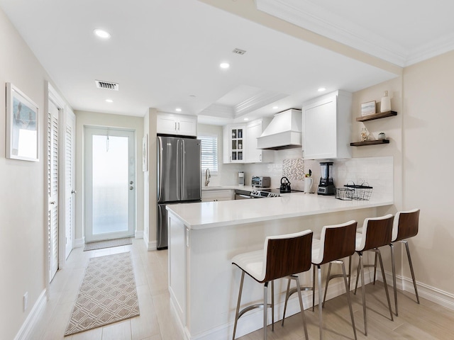 kitchen featuring premium range hood, stainless steel fridge, kitchen peninsula, white cabinets, and tasteful backsplash