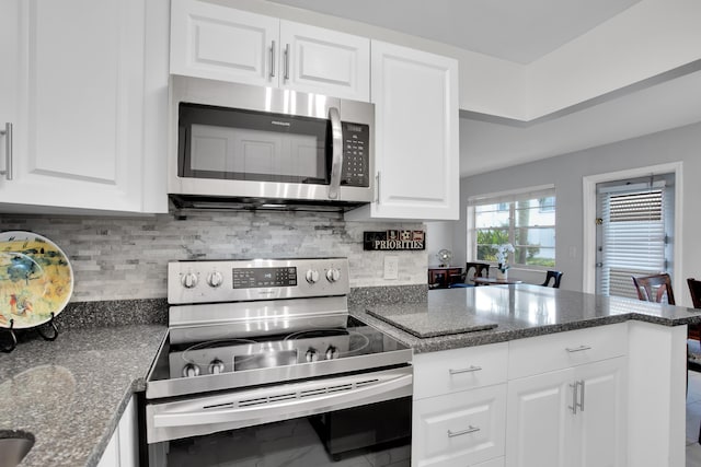 kitchen featuring white cabinets, decorative backsplash, dark stone countertops, a peninsula, and stainless steel appliances