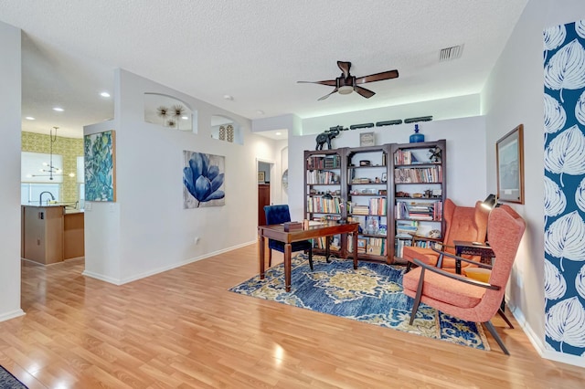 office featuring a textured ceiling, light wood-style flooring, visible vents, baseboards, and a ceiling fan