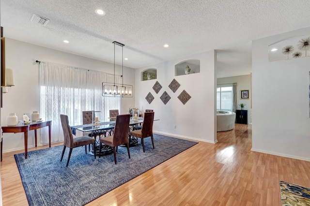 dining area featuring baseboards, visible vents, a textured ceiling, and light wood finished floors