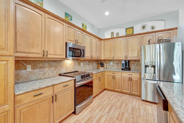 kitchen with light stone countertops, light wood-style floors, stainless steel appliances, and decorative backsplash