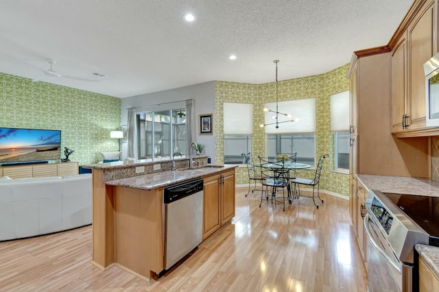 kitchen with appliances with stainless steel finishes, decorative light fixtures, a sink, and wallpapered walls