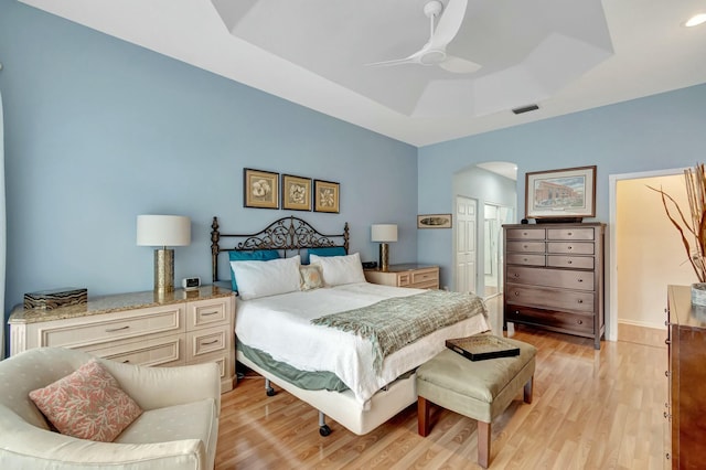 bedroom featuring visible vents, arched walkways, ceiling fan, a tray ceiling, and light wood-style floors