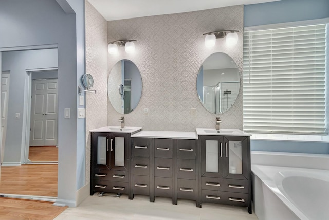 bathroom featuring a garden tub, wood finished floors, vanity, baseboards, and a shower stall