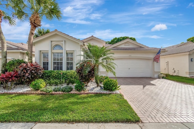 ranch-style home featuring a tiled roof, an attached garage, decorative driveway, a front lawn, and stucco siding