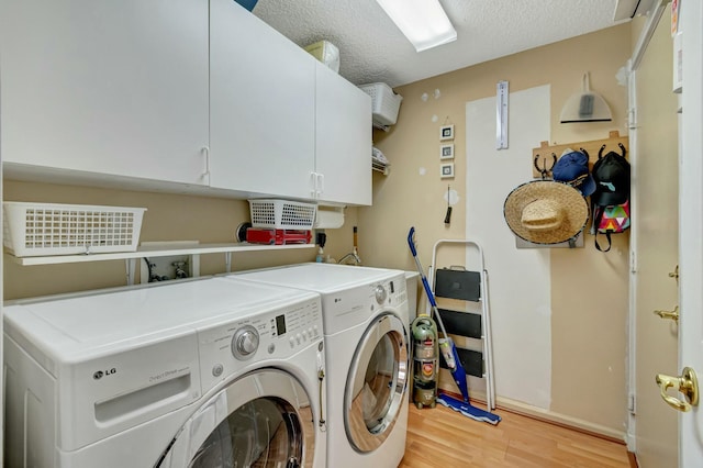 washroom featuring light wood finished floors, cabinet space, a textured ceiling, washer and dryer, and baseboards