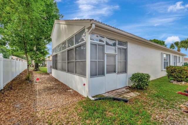 view of side of home featuring a sunroom, fence, and stucco siding