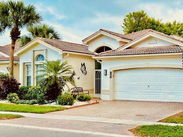 mediterranean / spanish-style house featuring a garage, a tiled roof, decorative driveway, and stucco siding