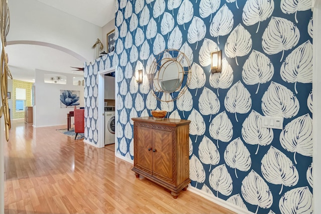 hall featuring washer / dryer, arched walkways, baseboards, and wood finished floors