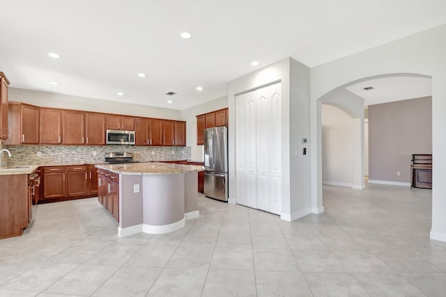 kitchen featuring stainless steel appliances, light stone counters, backsplash, a center island, and sink