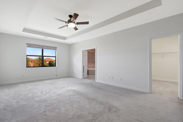 unfurnished bedroom featuring a raised ceiling, a walk in closet, light colored carpet, and ensuite bathroom