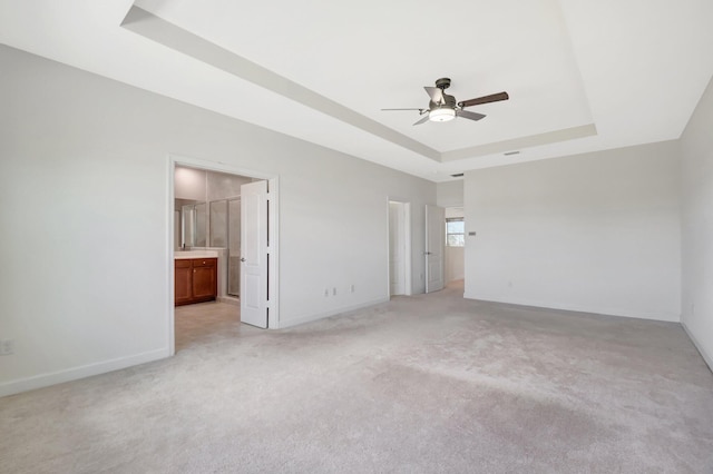 unfurnished bedroom featuring a tray ceiling, light colored carpet, and ensuite bath