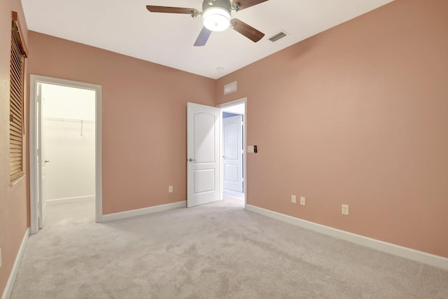 unfurnished bedroom featuring a closet, a spacious closet, light carpet, and ceiling fan