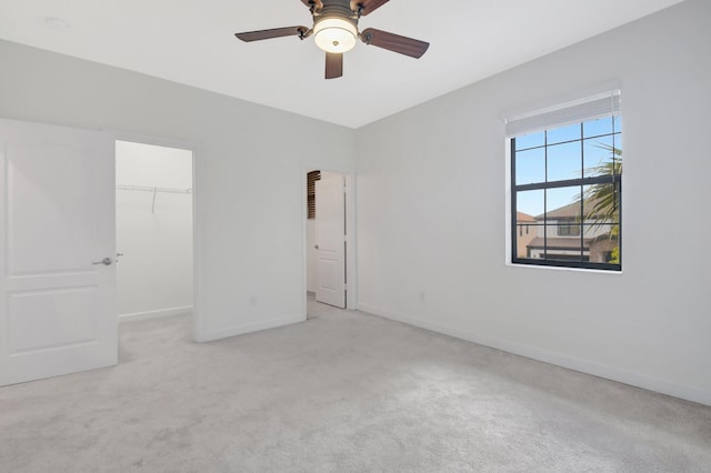 unfurnished bedroom featuring a spacious closet, light colored carpet, ceiling fan, and a closet