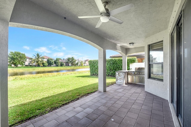 view of patio with ceiling fan, a water view, grilling area, and exterior kitchen