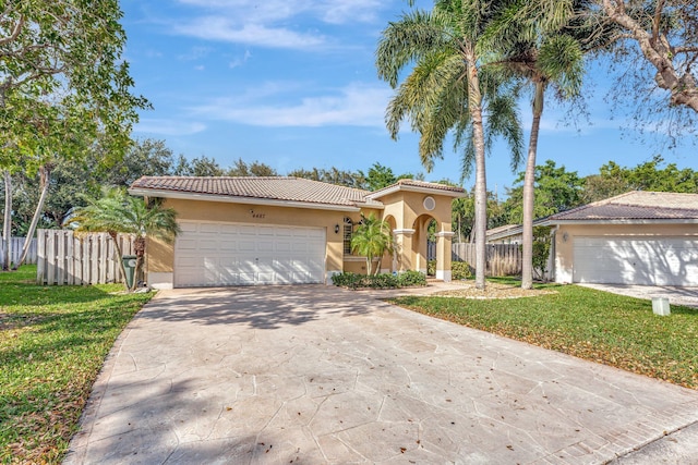 mediterranean / spanish home featuring a tile roof, fence, driveway, stucco siding, and a front yard