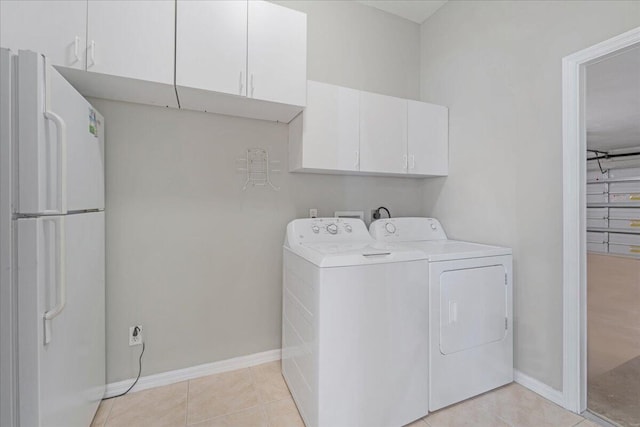 laundry area featuring washing machine and clothes dryer, light tile patterned floors, and cabinets