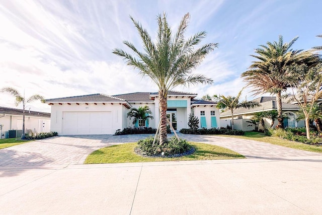 view of front facade with a garage, central AC unit, decorative driveway, and stucco siding